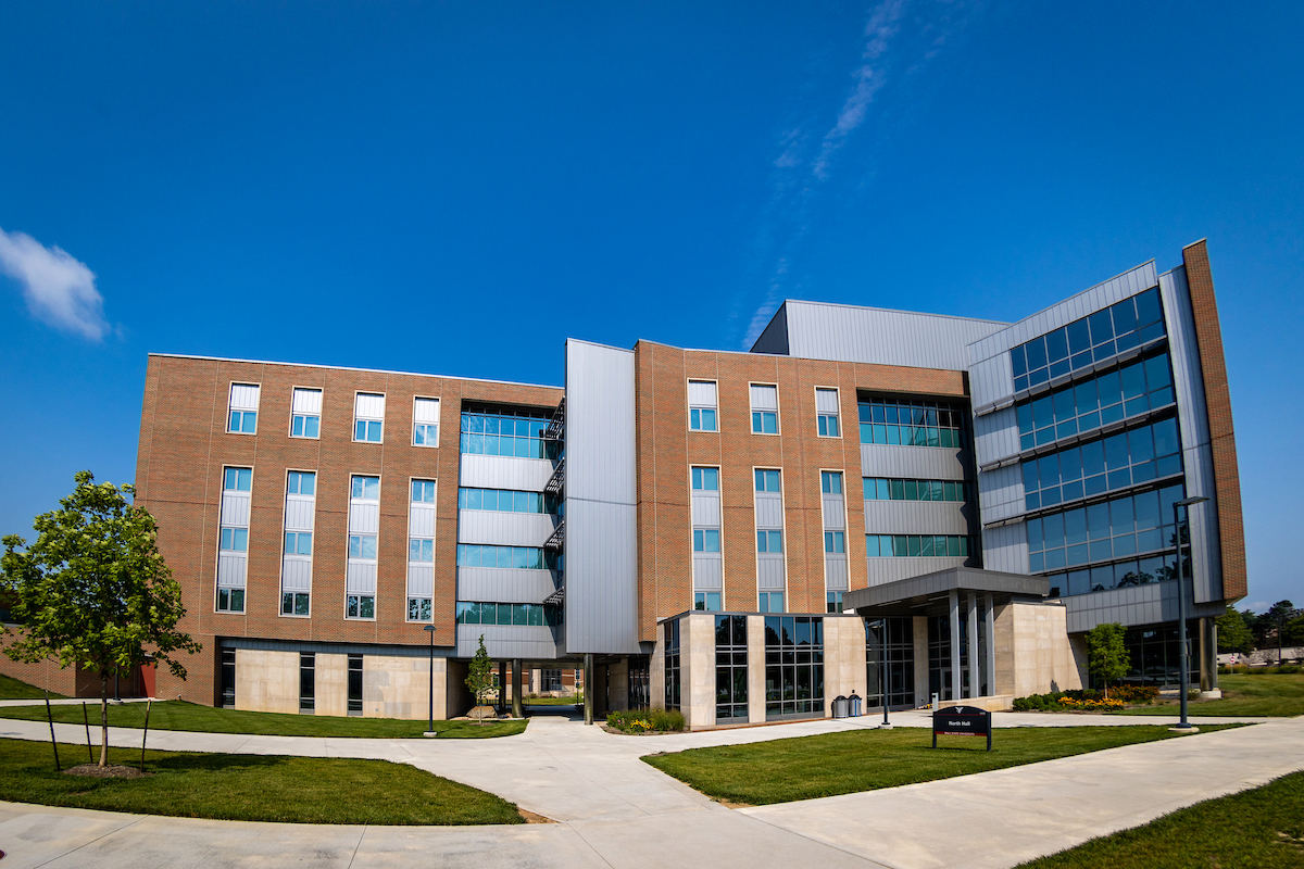 Multi-story, modern brick residence hall with open, grass plaza and sidewalks on Ball State University's campus.