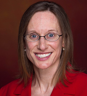 Smiling woman wearing glasses and a red blazer, posing against a dark studio background.