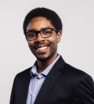 Jaden Sparks smiles for a professional portrait wearing glasses and a dark blazer.