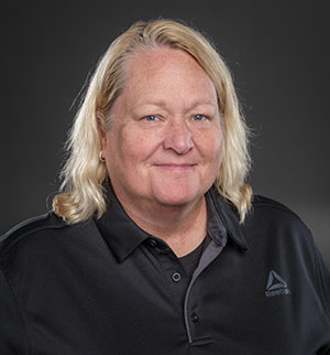 Leslie Miller posing in front of a dark gray background and wearing a black polo.