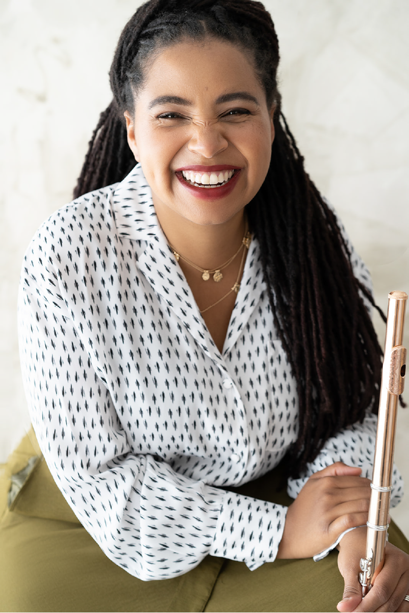 Dr. Jacqueline Cordova-Arrington smiles in a white and black button-down while holding a gold flute.