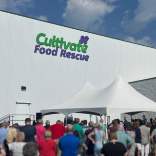 White building with Cultivate in green and Food Rescue in purple, people in front with white tent