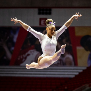 Gymnast in white Leotard leaping in Worthen Arena