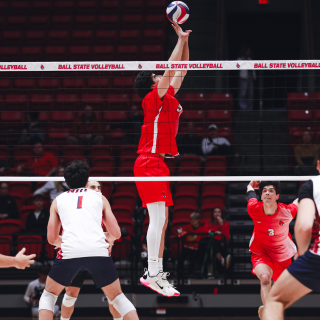 Men's Volleyball Player in red uniform setting ball, with net in front of him.