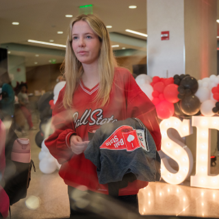 Student carrying a One Ball State Day t-shirt with OBSD light up letters with balloons around it in background