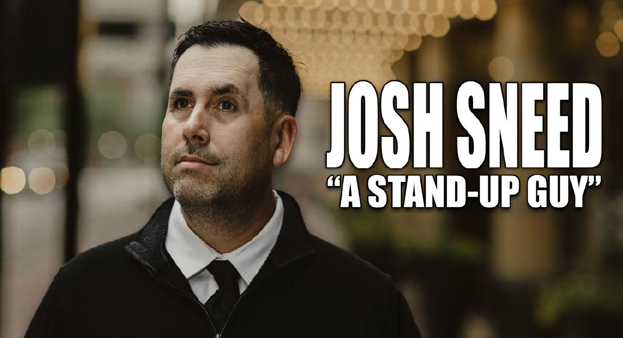 Comedian Josh Sneed stands before a lit up marquee outside. Image text reads, "Josh Sneed – A Stand Up Guy".