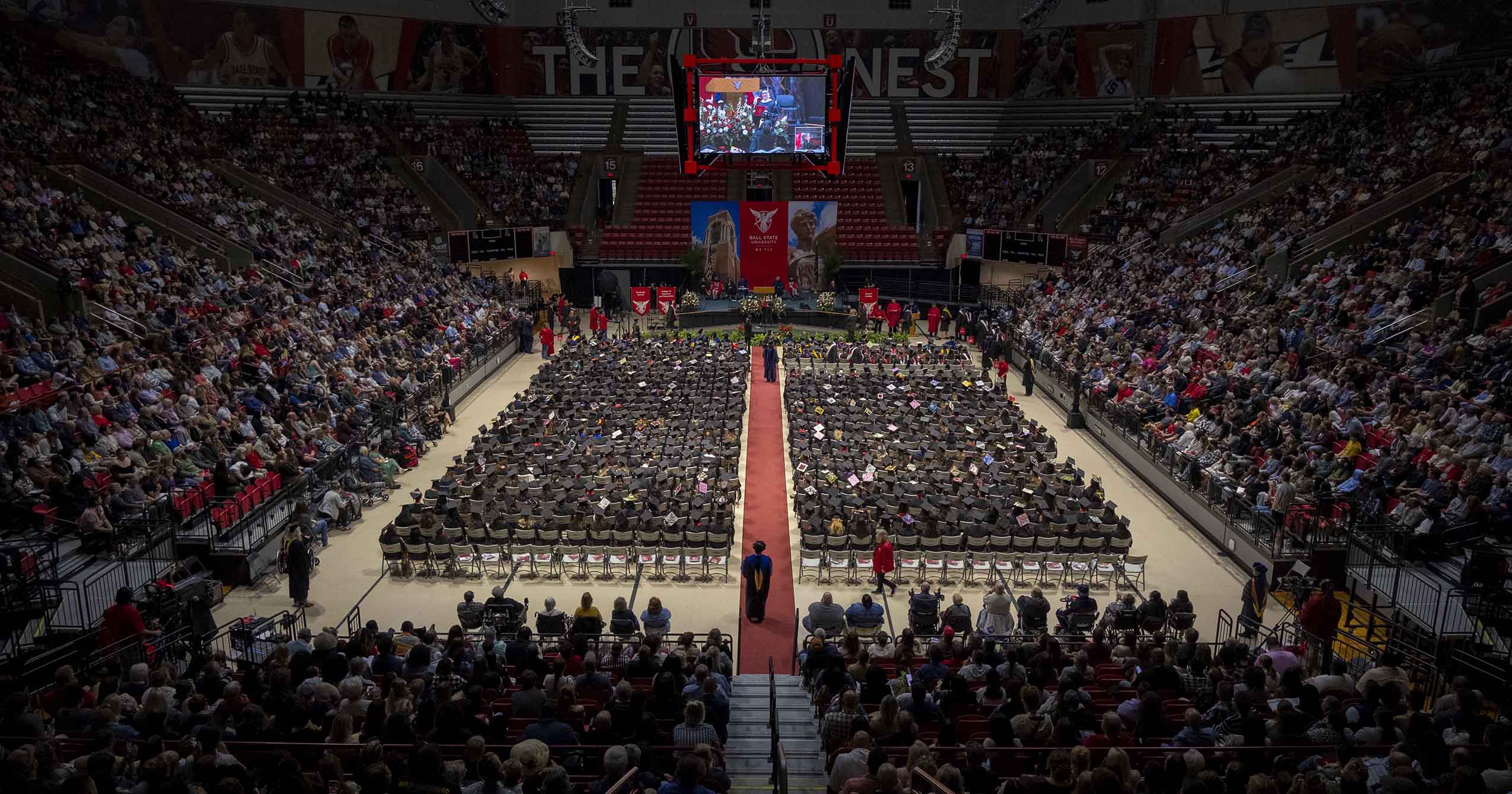 Wide view of Ball State graduates seated on the floor of Worthen Arena, with guests filling the stands during a Commencement ceremony.