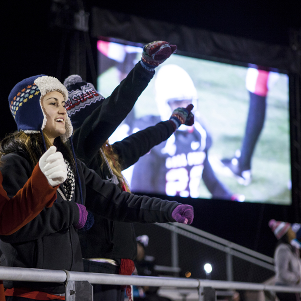 Fans cheer on the Cardinals as displayed by a video screen behind them