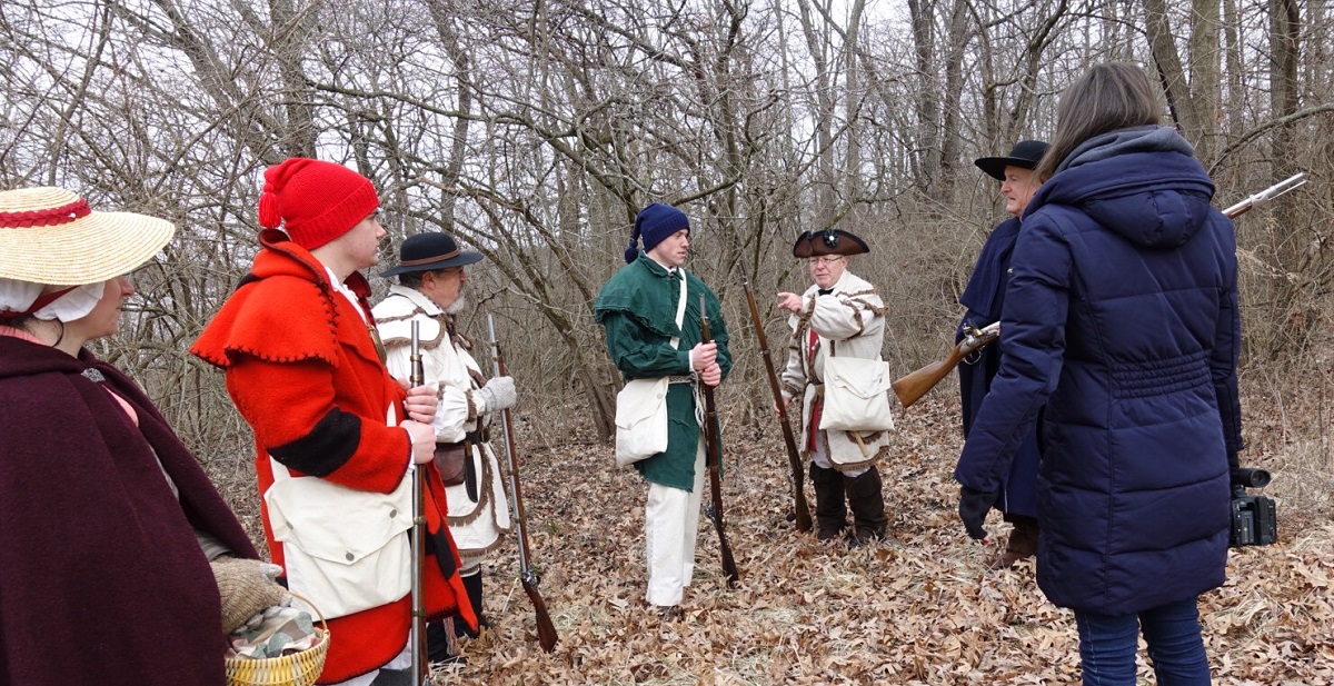 The student actors, videographer and Sons of the American Revolution members collaborate on how best to film the scene.