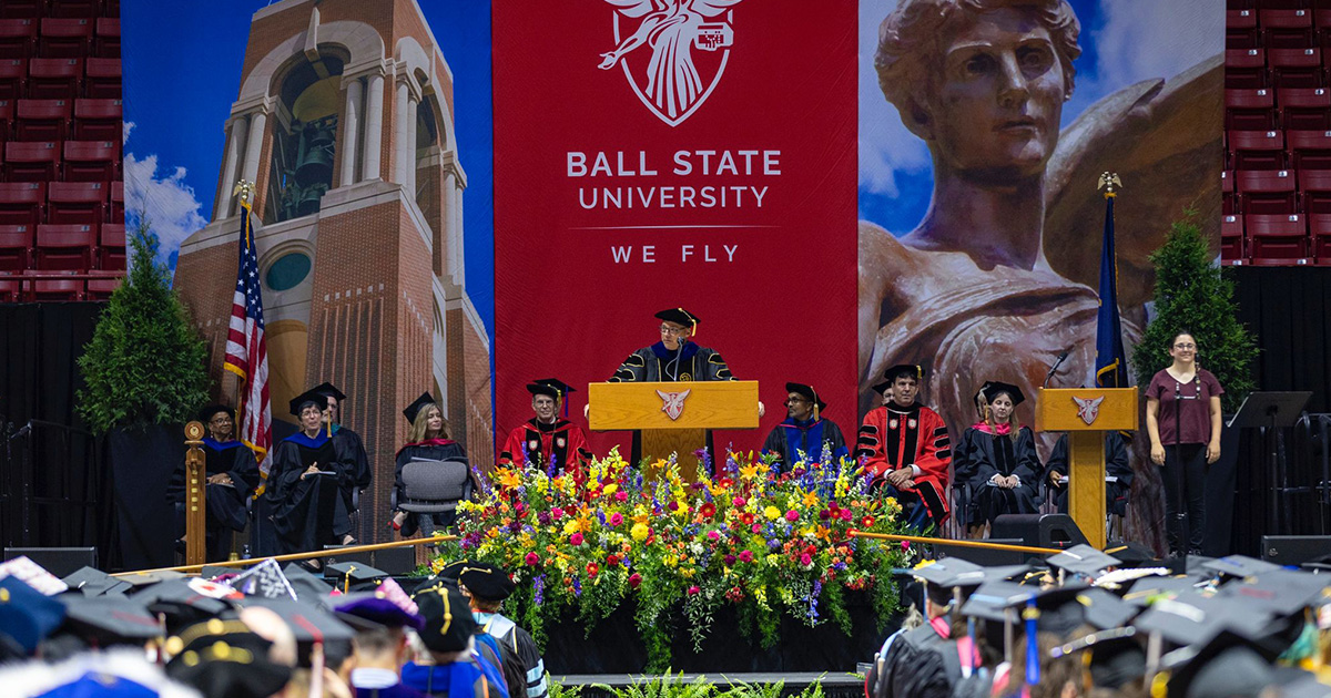 President Mearns speaking at a podium on a stage at the Summer 2024 commencement ceremony