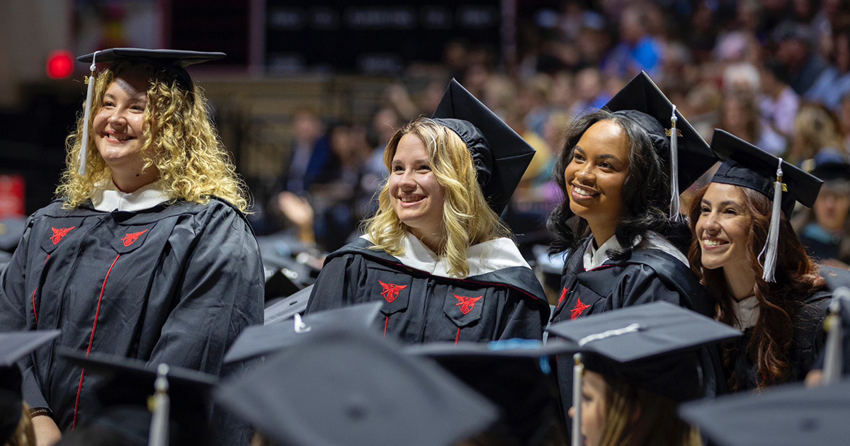 Group photo of four graduates smiling at the commencement ceremony