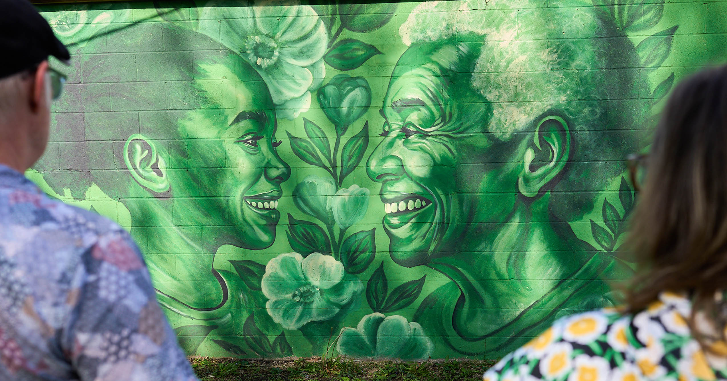 Visitors look at a green mural of two smiling faces surrounded by flowers and leaves at ArtRize in Muncie.