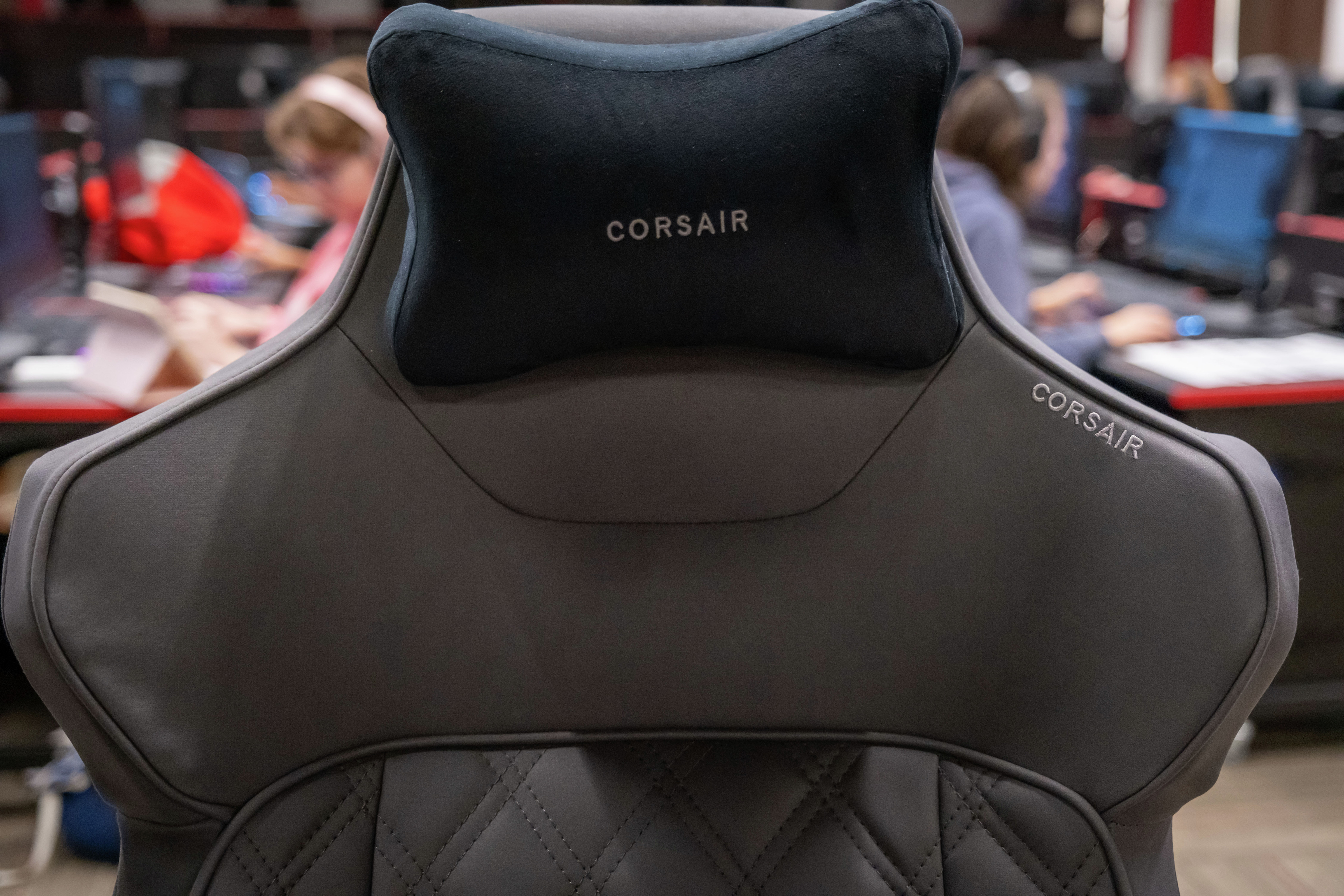 A Corsair gaming chair in the Ball State Esports Center, with students working at computers in the background.