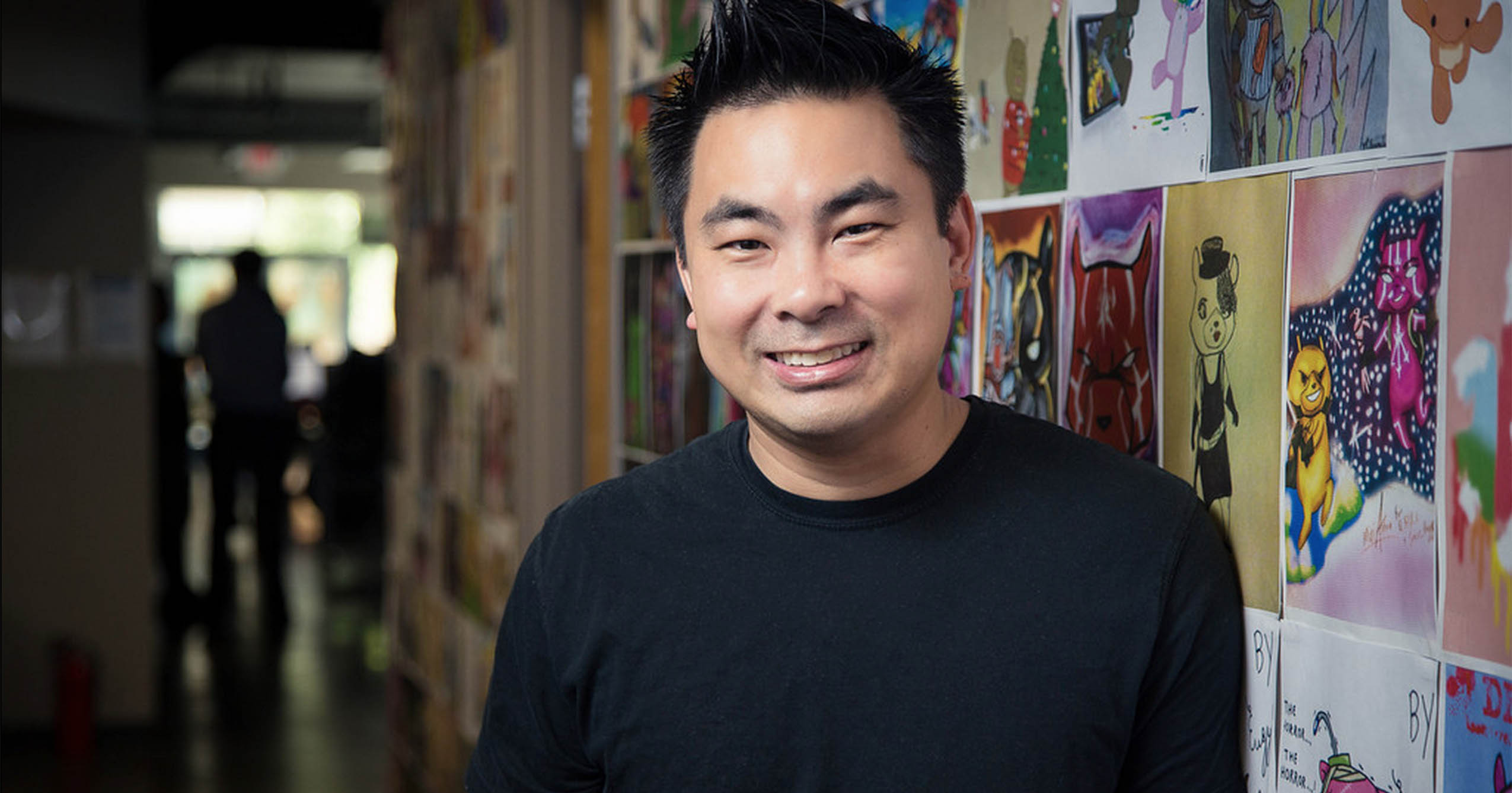 Ball State alumnus Ben Vu smiles beside a wall displaying colorful character artwork.