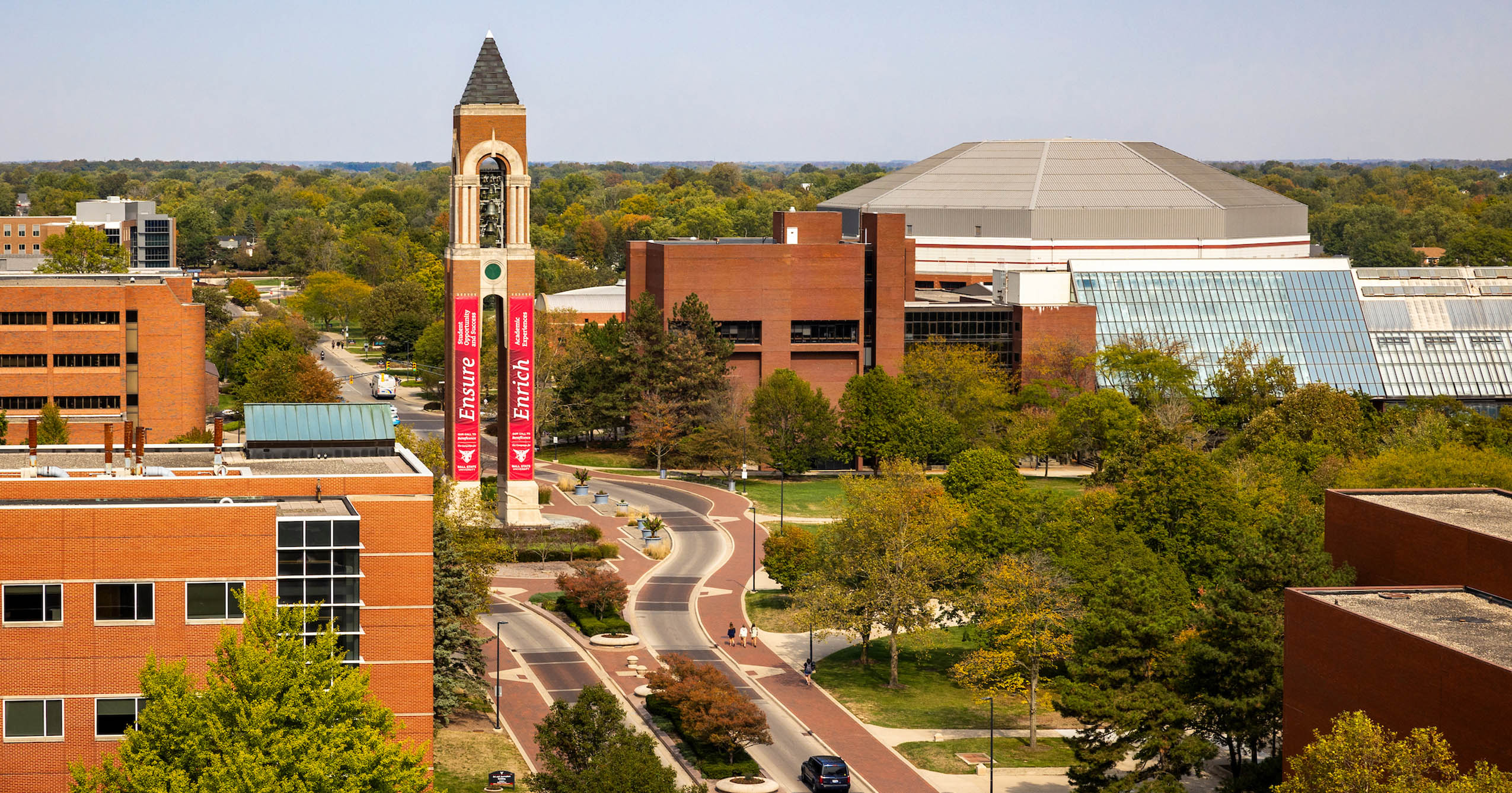 Elevated view of Ball State’s campus centered on Shafer Tower with red Our Call to Beneficence campaign banners displaying pillar themes.
