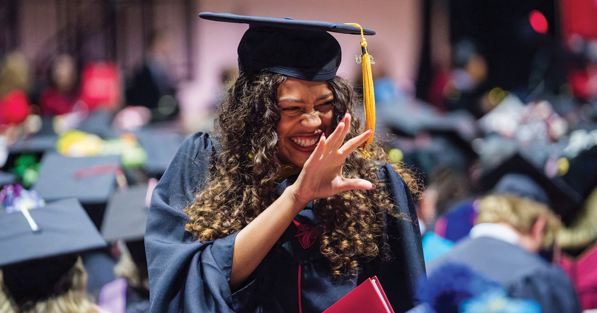 Graduate laughs and waves after receiving her diploma cover.