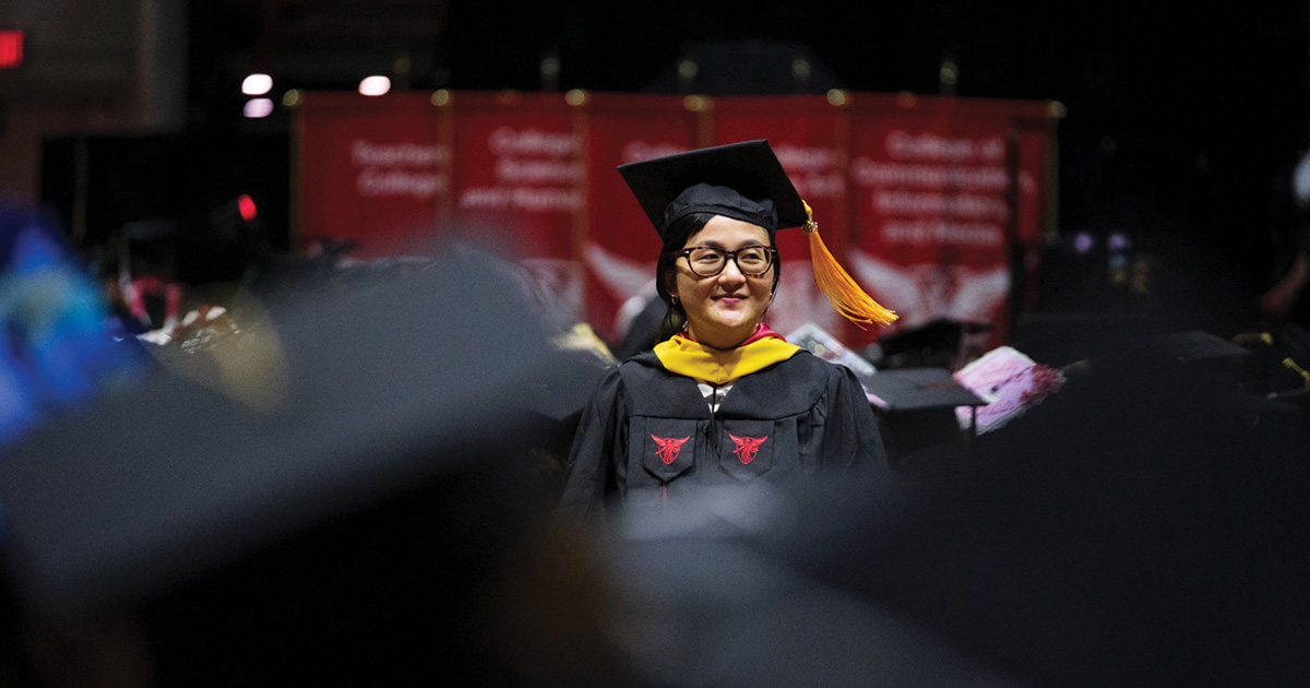 Graduate stands among rows of seated graduates before the commencement ceremony.