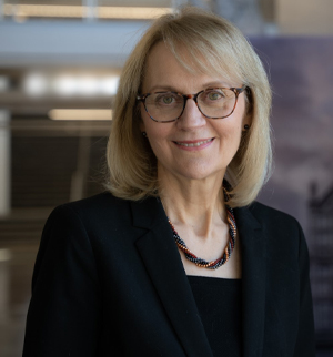 Headshot of Dean Cathy DuBois, a blond woman in a dark suit wearing glasses and complimentary jewlery.