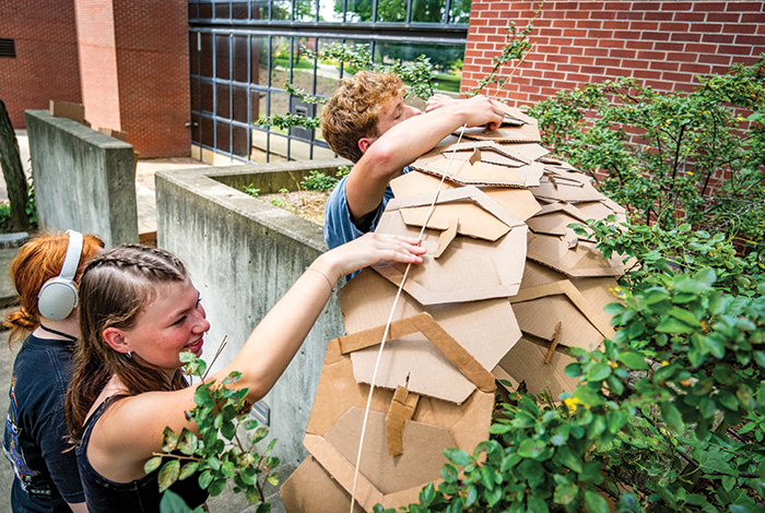 Students work together to assemble a large cardboard structure outdoors.