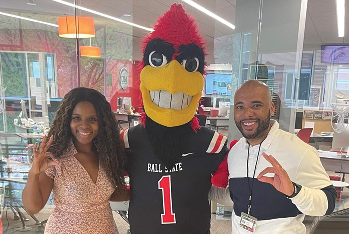 Kirsten Norwood and another staff member pose with Charlie Cardinal, making the Beneficence hand sign.