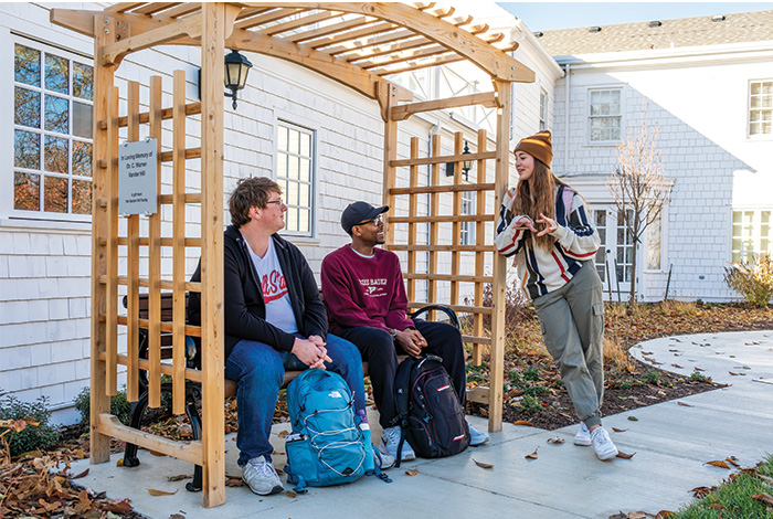 Three students talk beside a wooden pergola outside the Ball State Honors House.
