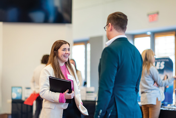 A woman holding a portfolio talks with a man during a professional networking event.